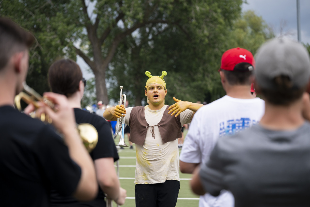 A band member dressed as the Shrek character gives instructions to peers.