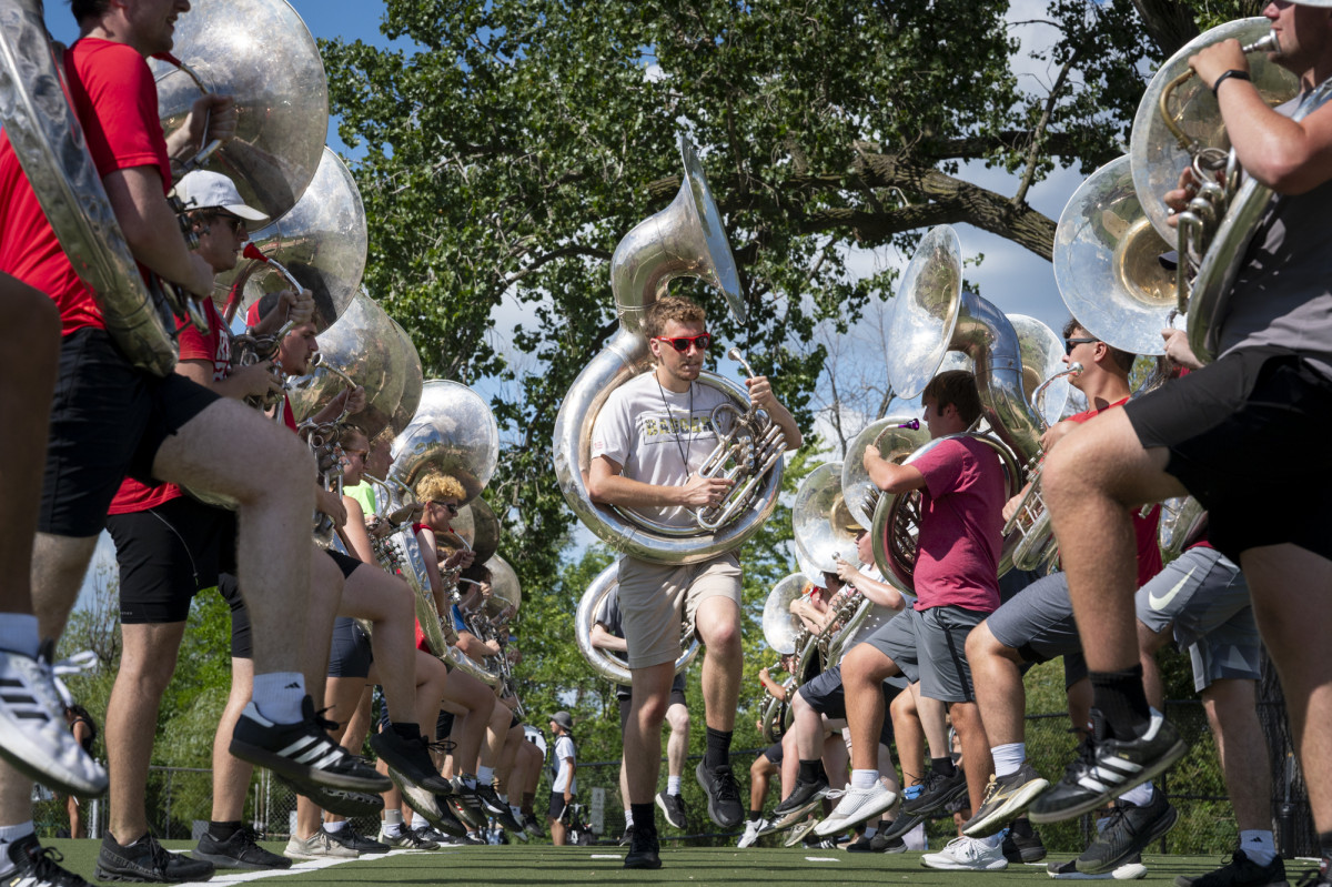 Members of the UW Marching Band tuba section practice marching with high-knee strides outdoors on an athletic field.