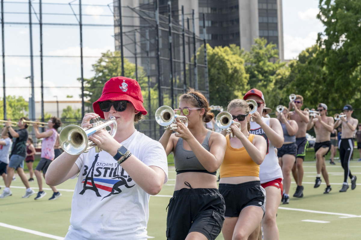 Trumpet players practice marching on a turf playing field.