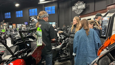 Students talk to a salesperson inside a Harley-Davidson dealership filled with motorcycles.