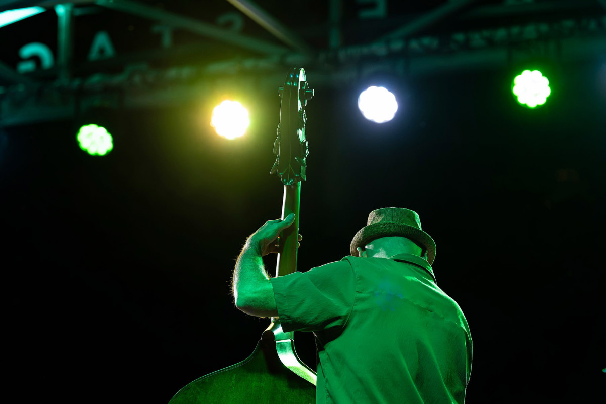 A bass player wearing a hat under green stage lights