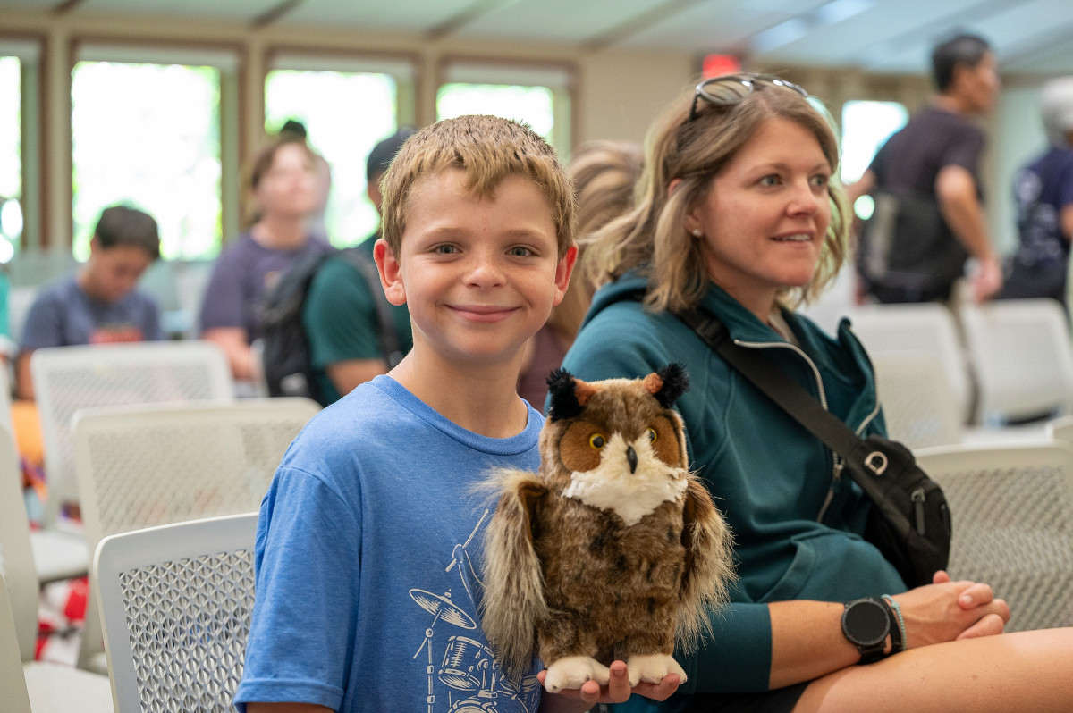 A young boy holds a stuffed toy owl and smiles for the camera.