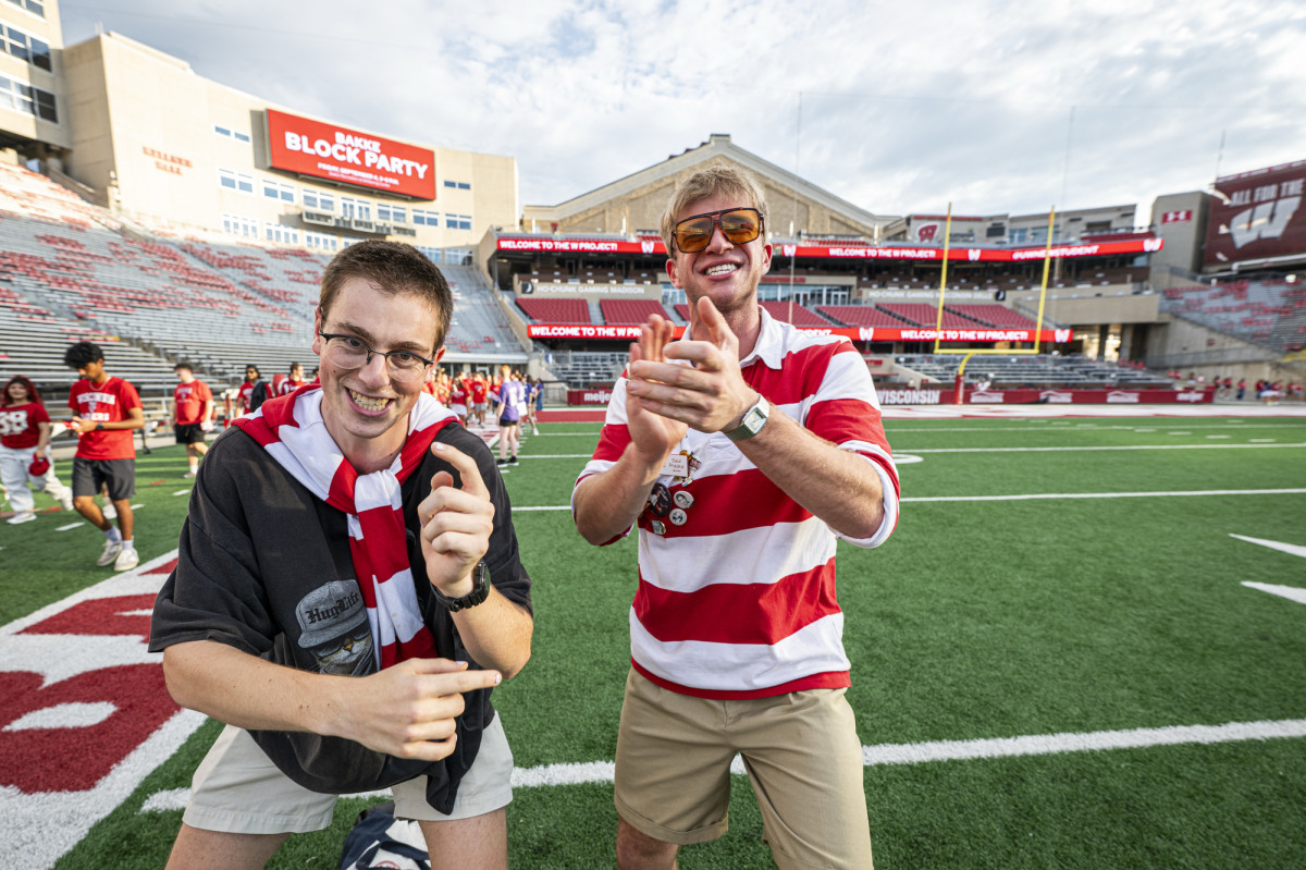 Two students wearing red and white striped shirts clap for the camera as they enter Camp Randall Stadium for an orientation event.
