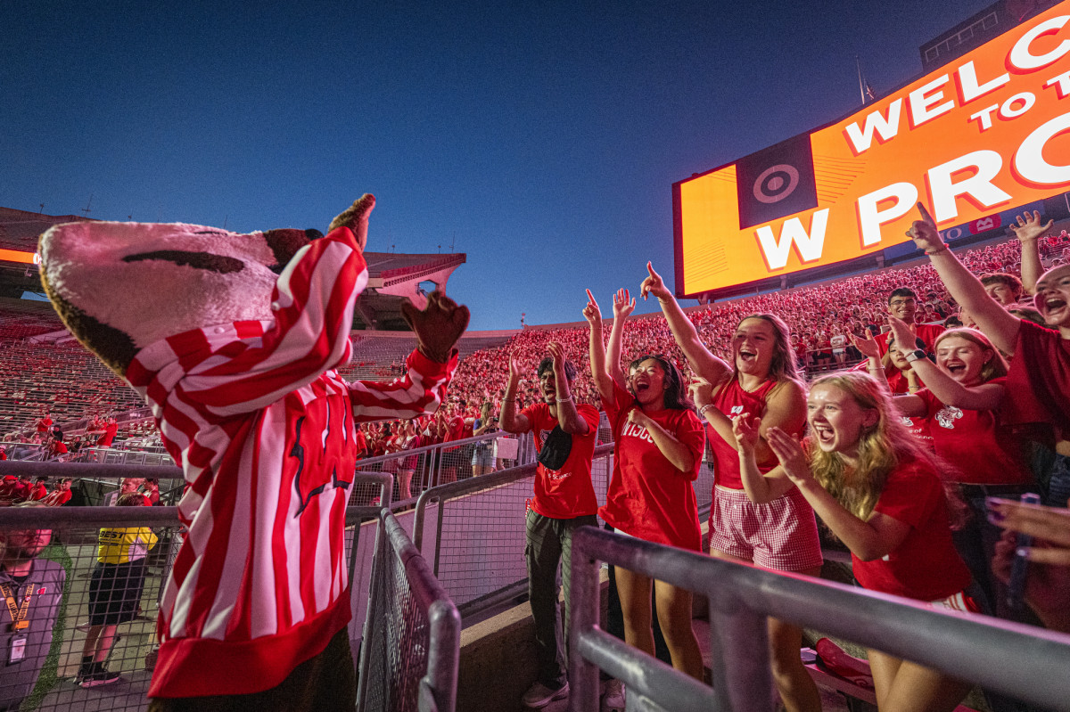 Mascot Bucky Badger raises his hands as he leads enthusiastic UW students in a cheer under the lit-up W Project screen at Camp Randall Stadium.