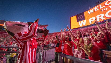 Mascot Bucky Badger raises his hands as he leads enthusiastic UW students in a cheer under the lit-up W Project screen at Camp Randall Stadium.
