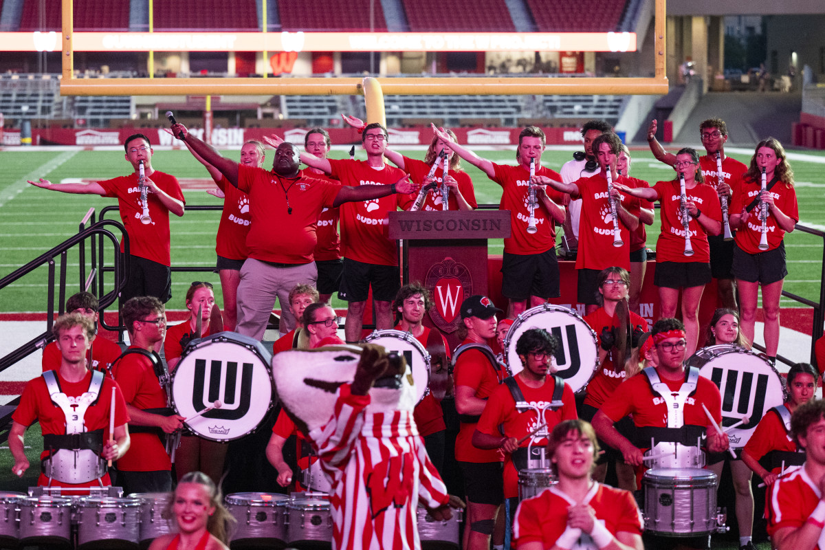 Pompey, surrounded by UW Marching band members, stands on a platform and leads the crowd in the singing of Varsity.