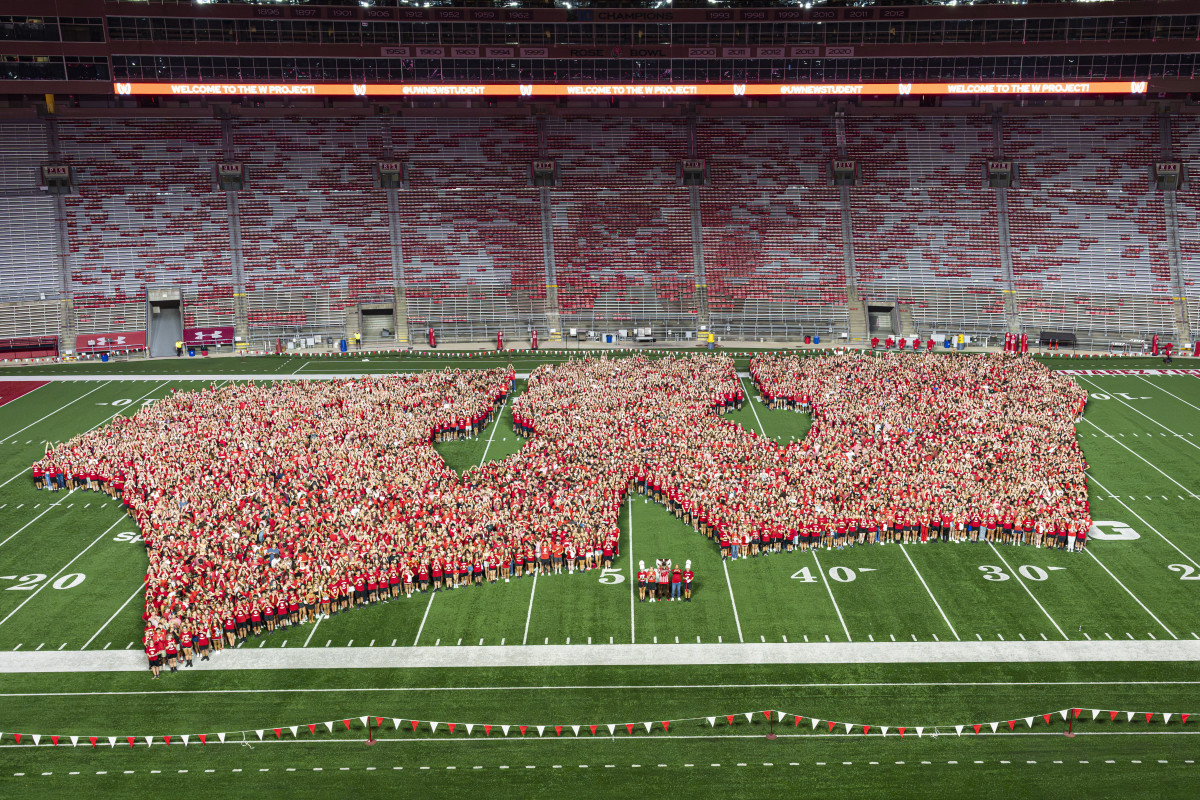 An overhead wide shot of thousands of incoming students wearing red shirts assembled on the field at Camp Randall Stadium to form a massive Motion W logo.