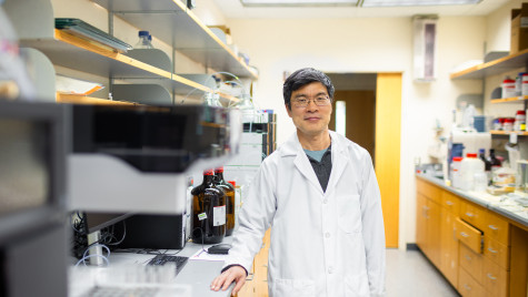 Wearing a white lab coat, Tang poses for a picture in his lab.