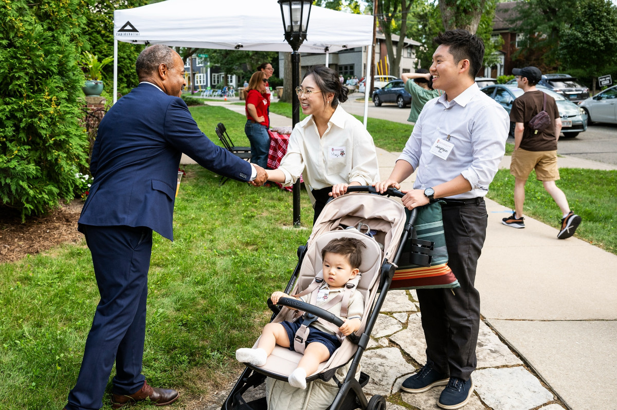 Interim Chancellor Wilcots shakes the hand of an attendee who arrives at Olin House with her husband, who is pushing their child in a stroller.