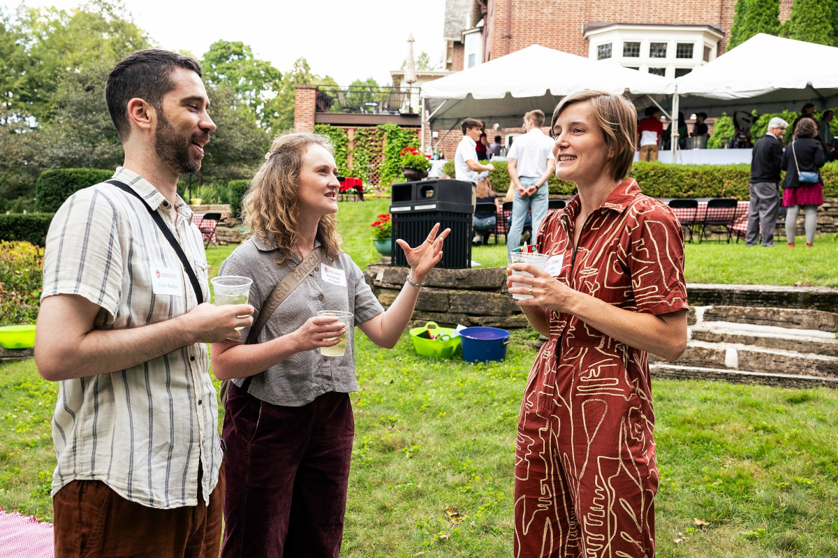 Three people, including two new UW faculty members, hold drinks and talk while standing on a backyard lawn.