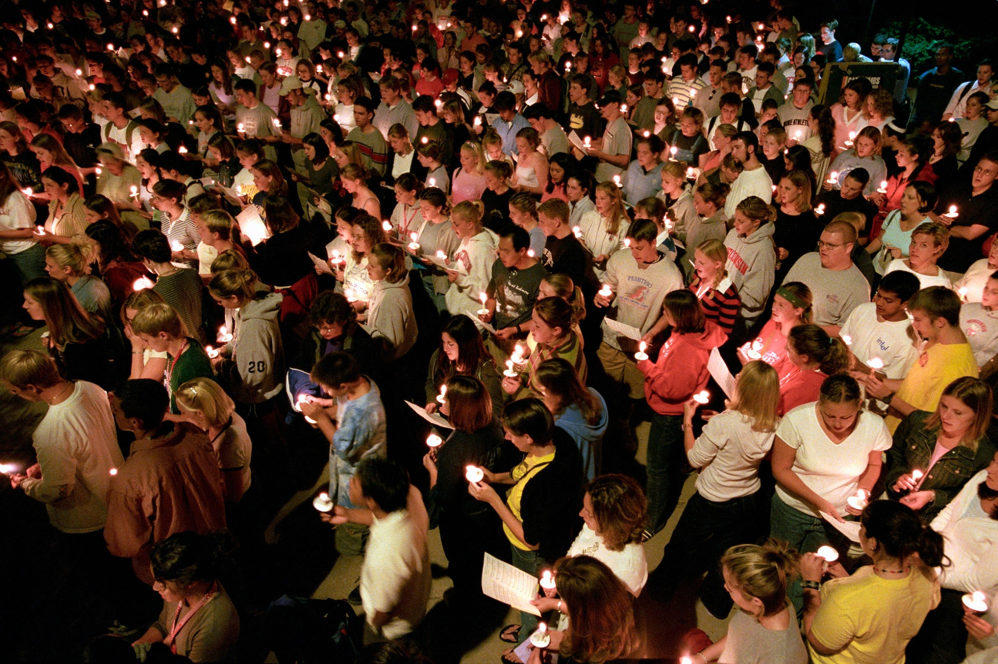 Dozens of people gather shoulder to shoulder holding candles in the dark for a vigil.