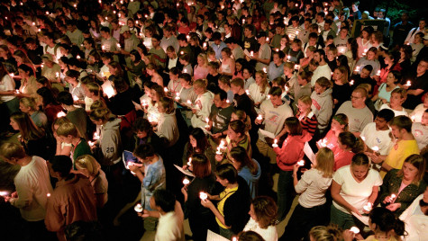 Dozens of people gather shoulder to shoulder holding candles in the dark for a vigil.