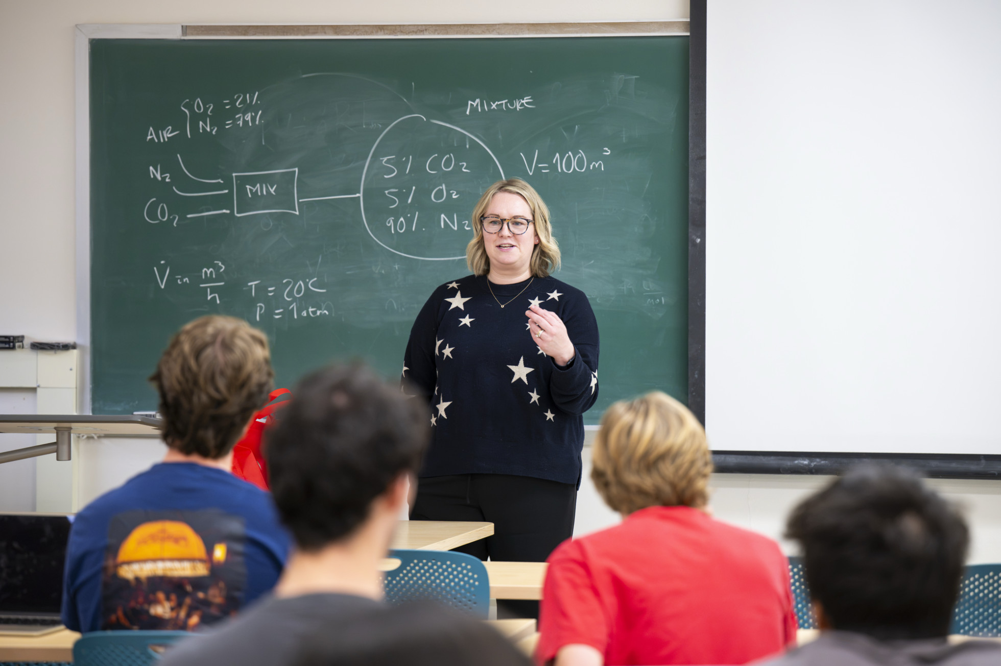 Eimear Robertson stands and talks in front of a class, with a chalkboard in the background. 