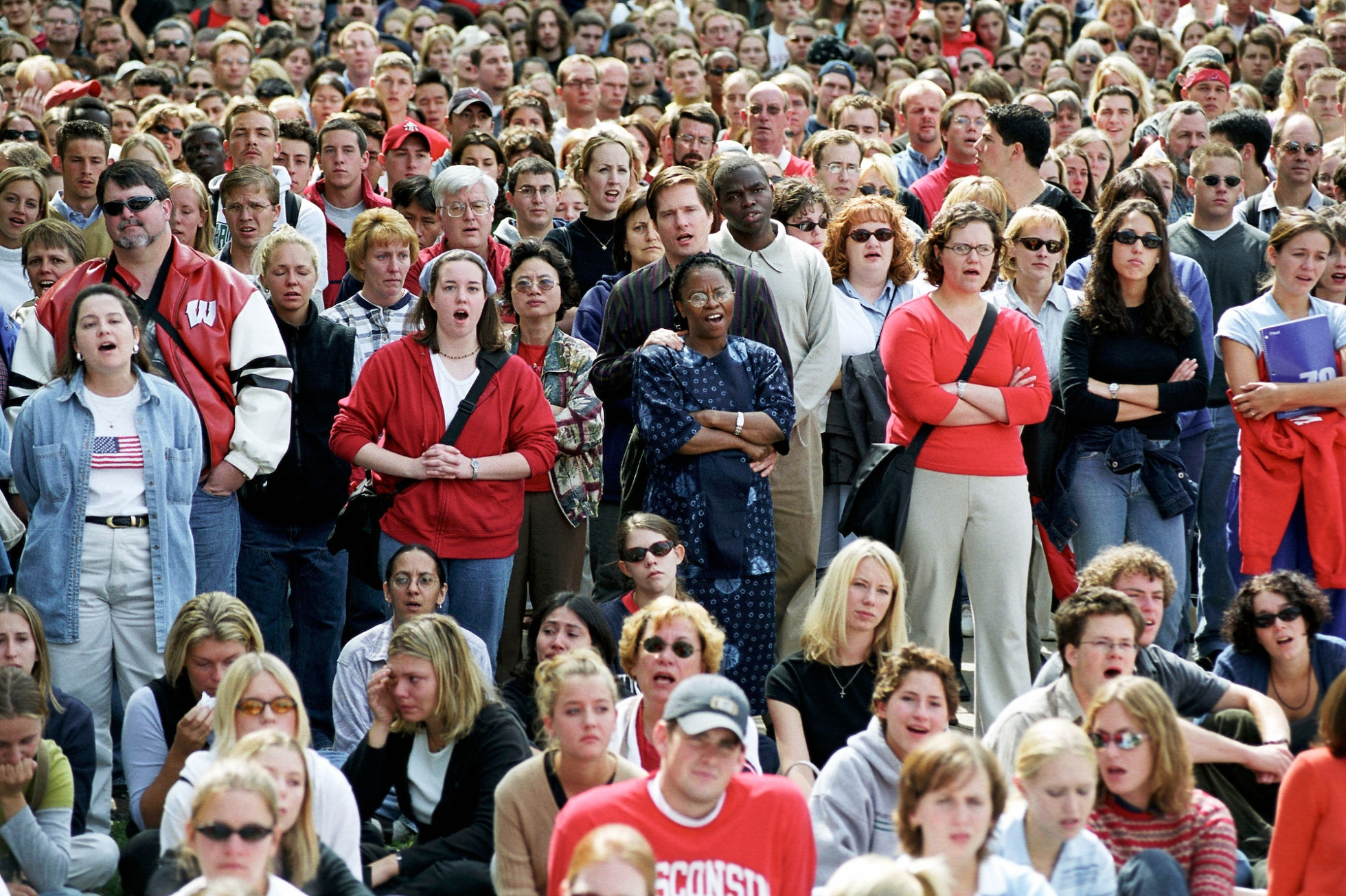 A crowd of people, both standing and sitting, sing and show emotion together.