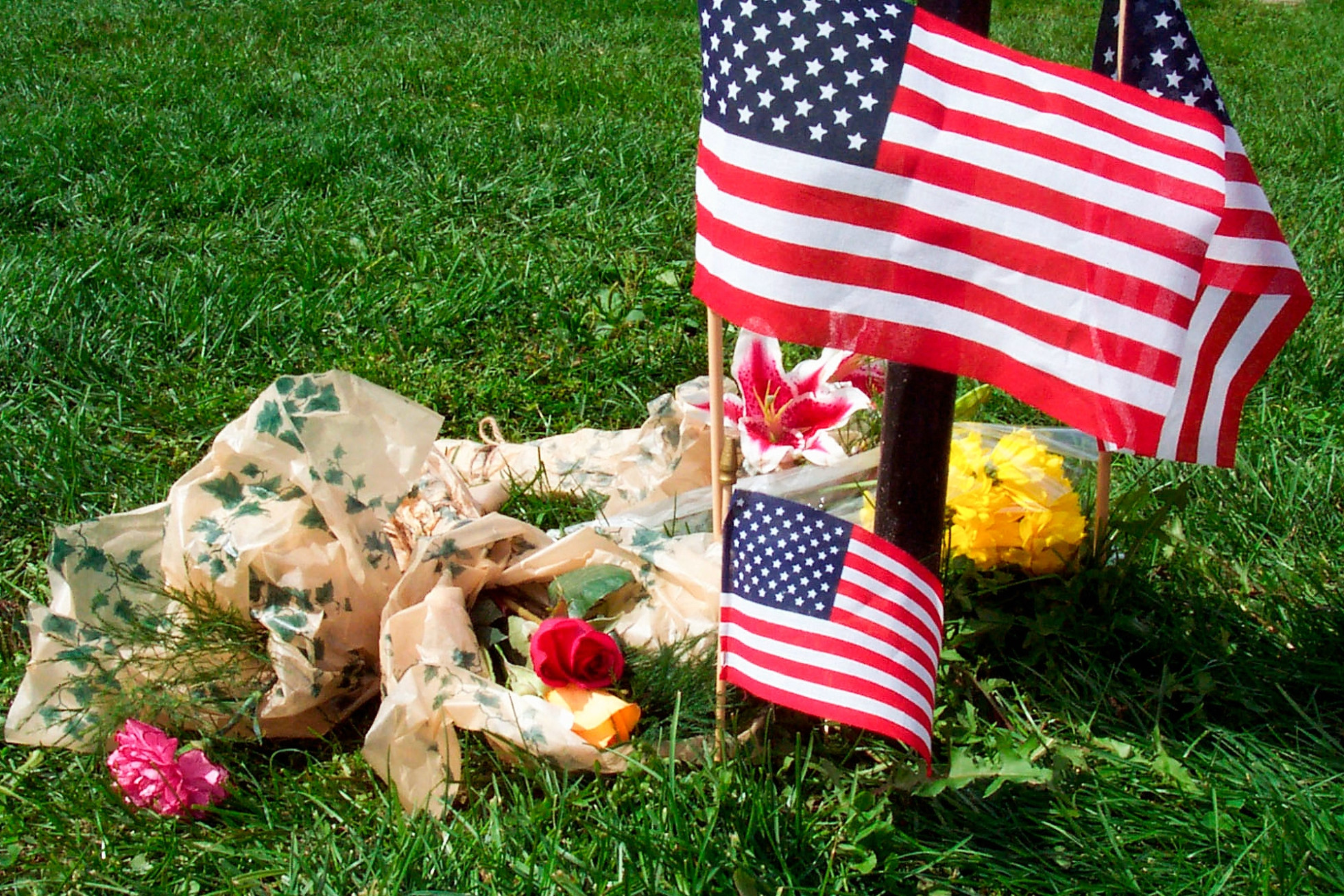 Small American flags and flower arrangements are placed on grass.