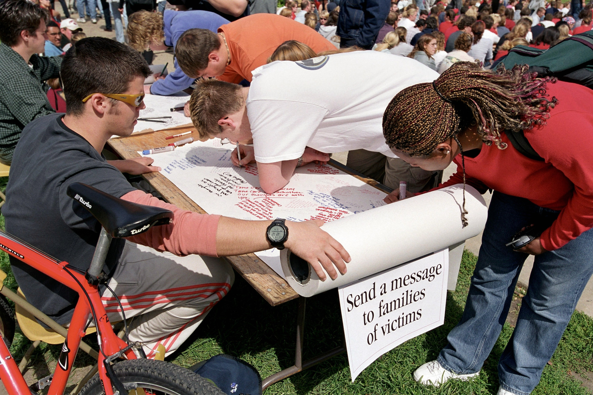 People use markers to write on large paper rolls, with a sign that states "Send a message to families of victims."