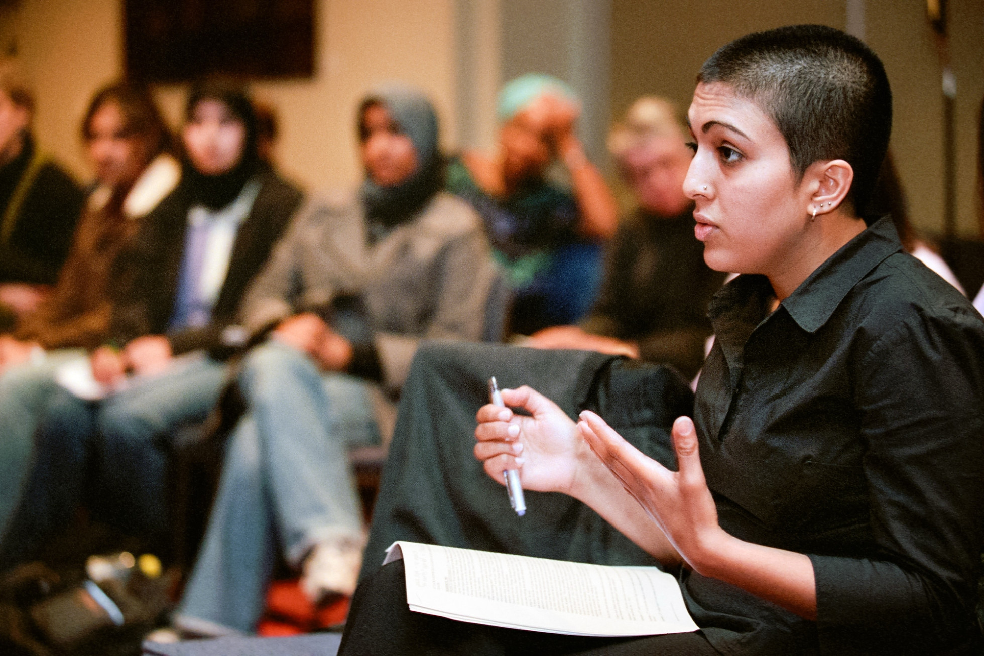 A woman gestures with her hands while speaking, in a room full of people.