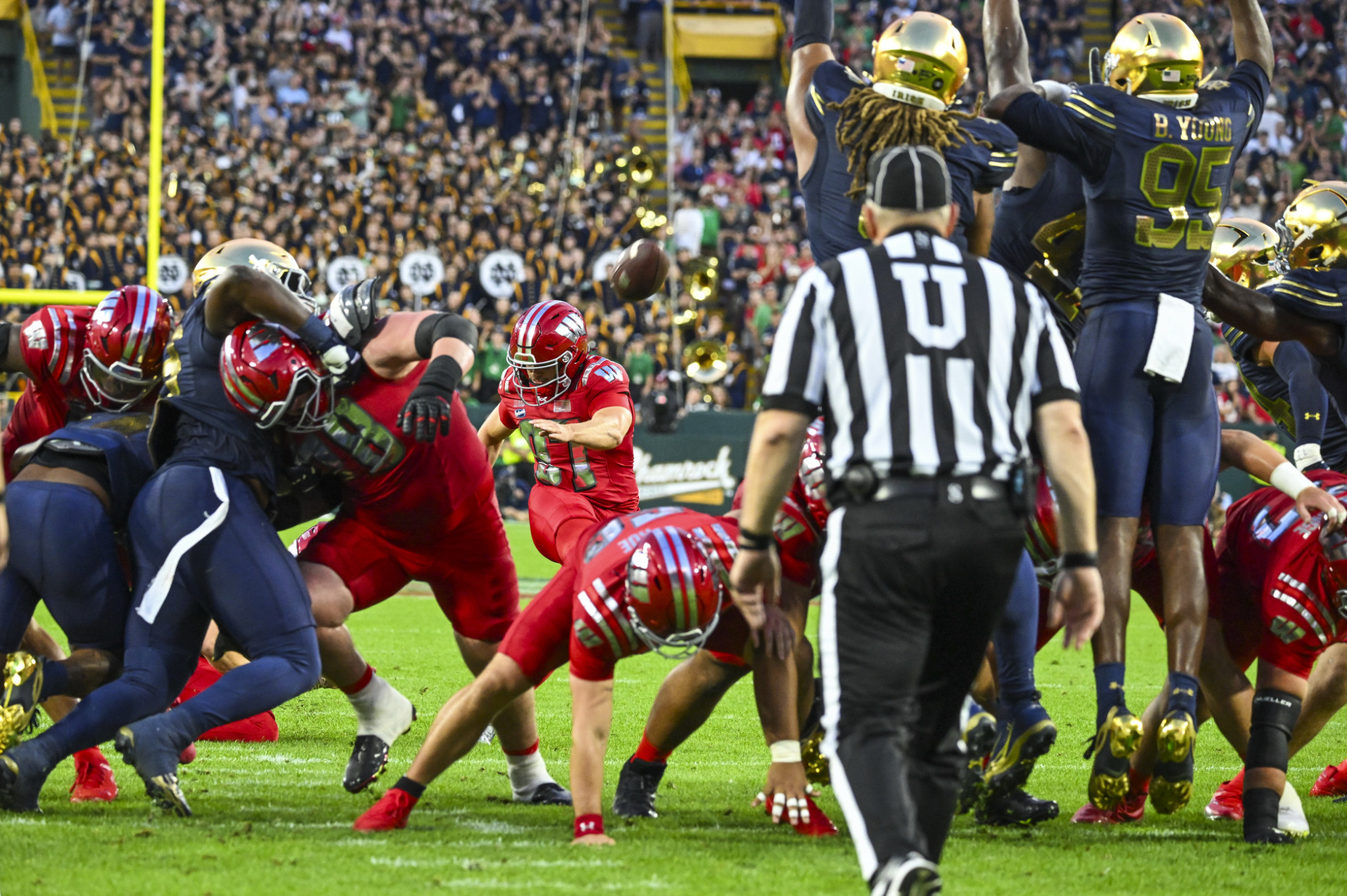 A Badger player kicks a football in front of a scrum of linemen.  
