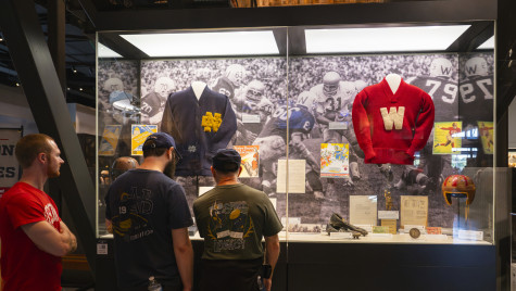 Three people look at a glass display that shows early football uniforms and other artifacts from Wisconsin and Notre Dame.