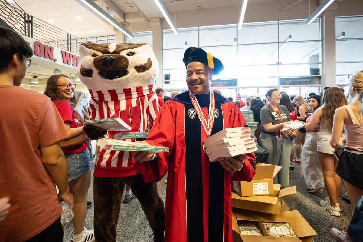 Interim Chancellor Eric Wilcots and Bucky Badger hand out books in the Kohl Center concourse.