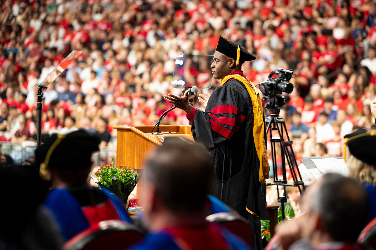 Professor Percival Matthews, in academic regalia, addresses the crowd from behind a wooden podium.