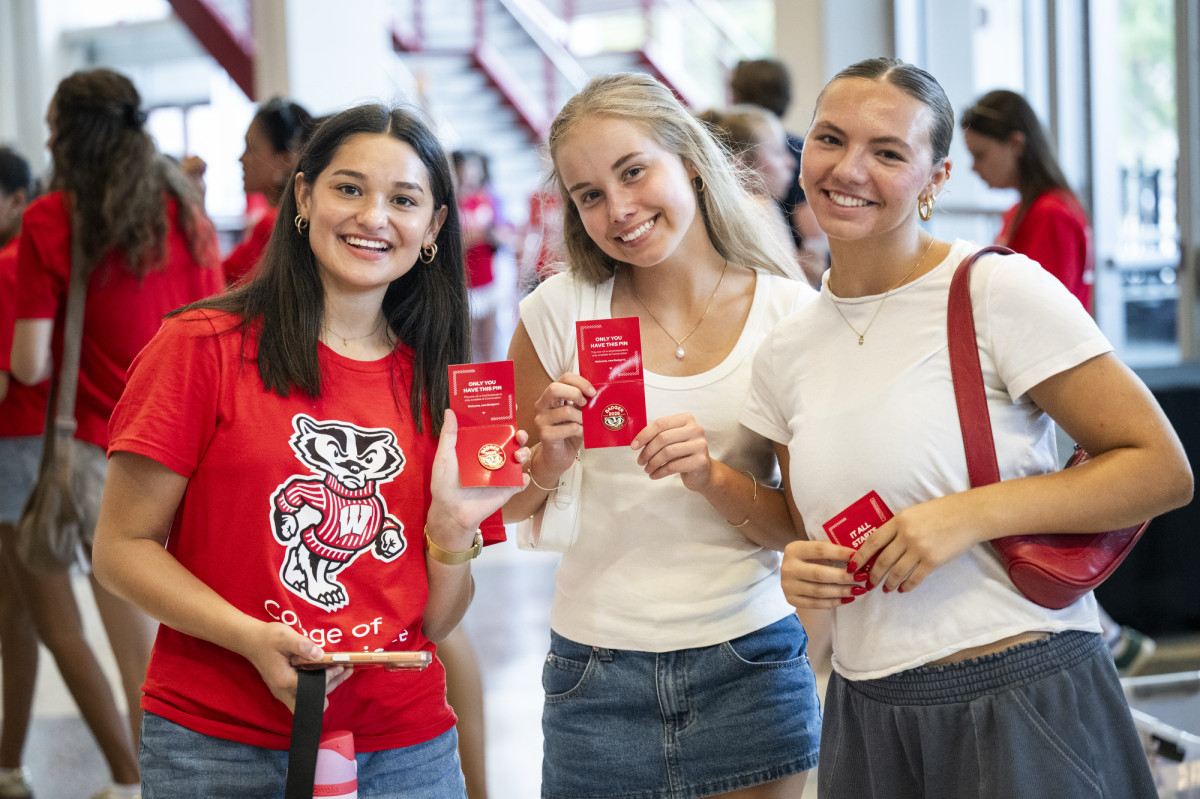Three students smile and pose with commemorative pins.