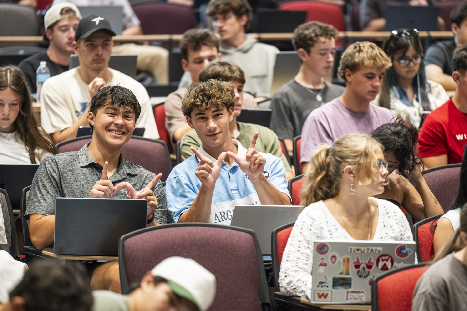 Two students in a lecture hall hold up the W sign. 
