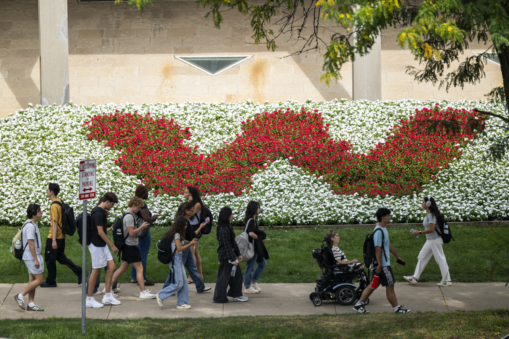 Students pass by the red W made from flowers on the UW–Madison campus.