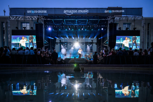 Kane Brown performs on a large stage, with a crowd and fountain in the foreground.