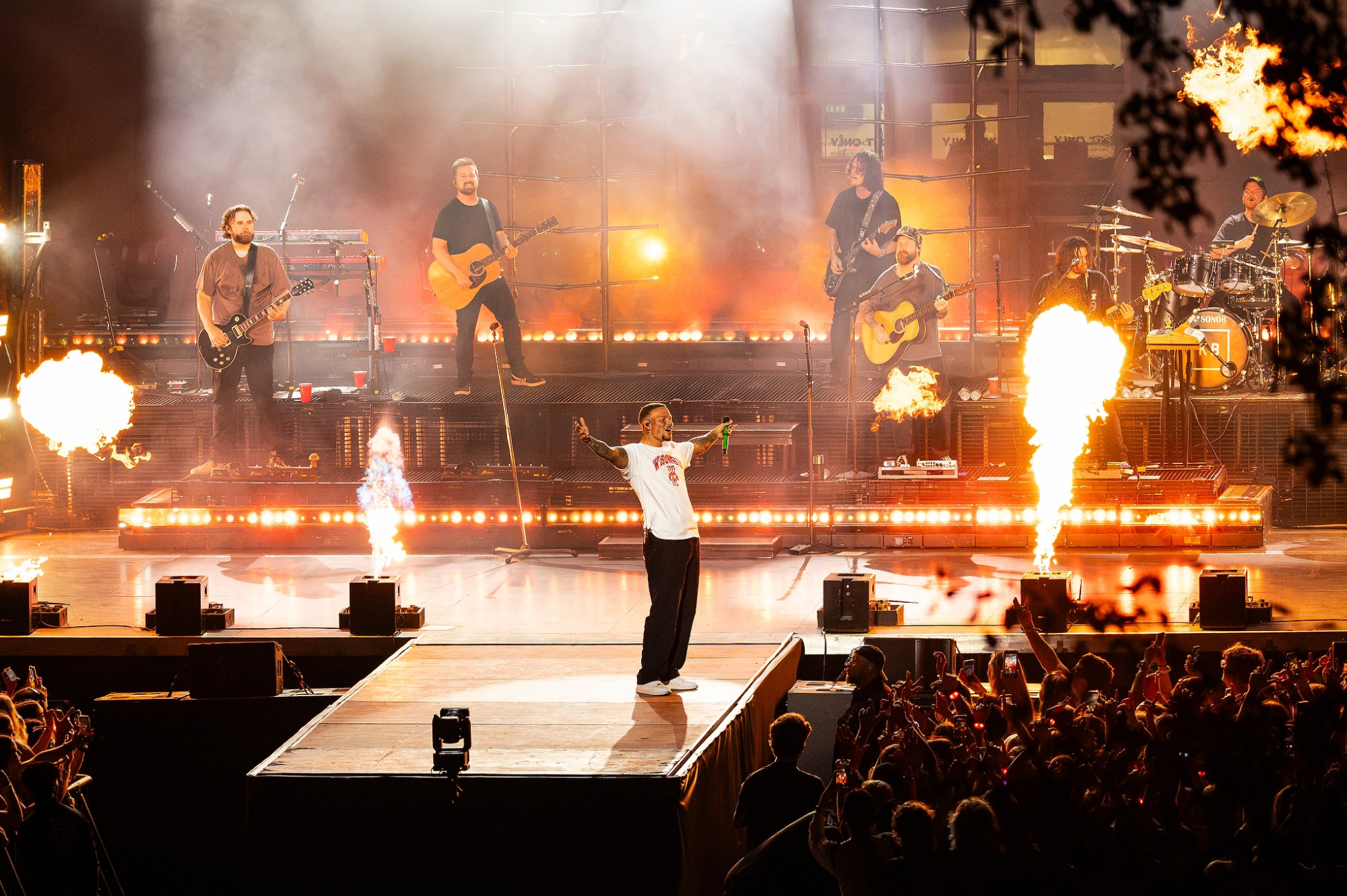 Kane Brown opens his arms while performing on stage, with pyrotechnic flames going off.