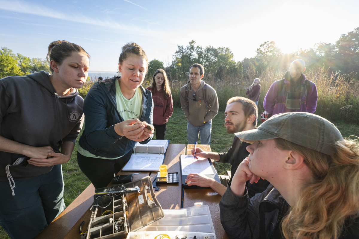 A group of people gather around a table to look at a volunteer holding and talking about a bird. 