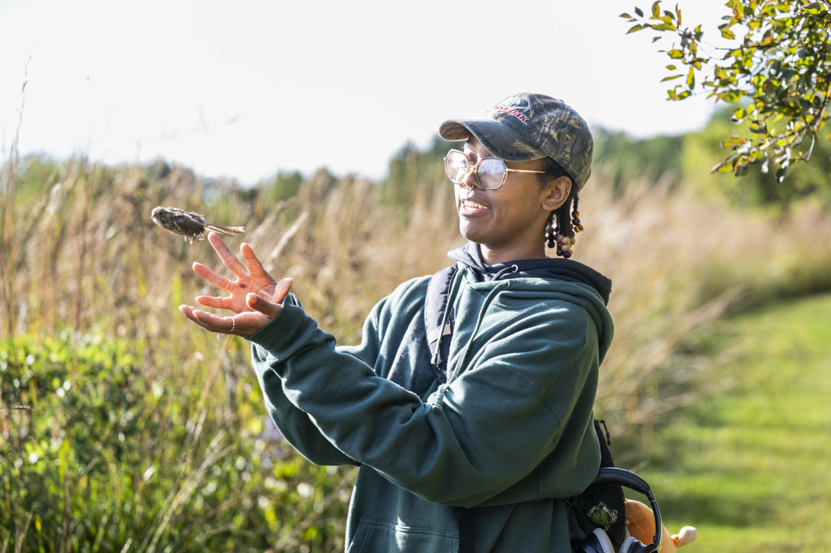 A volunteer lifts their arms to release a bird that flies out of their hands. 