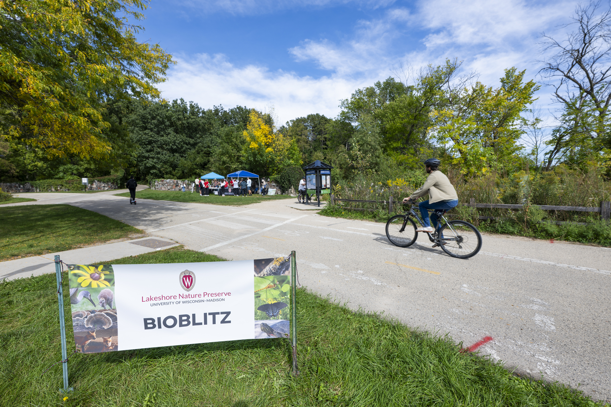 A bicyclist rides past a sign that reads Bioblitz outside the entrance to Picnic Point. 