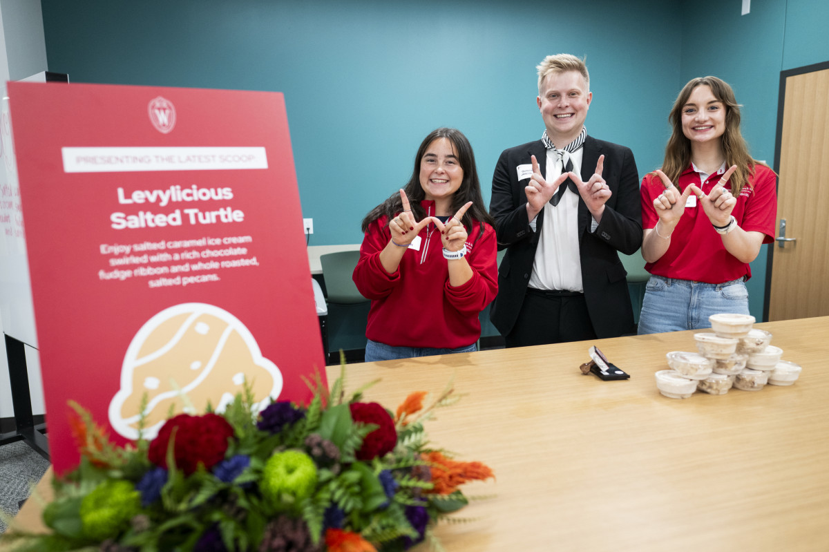 Three people hold up the W sign in front of a sign for Levylicious Salted Turtle ice cream.