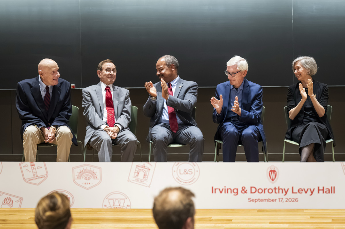 Marv and Jeff Levy sit on stage with other dignitaries applauding them.