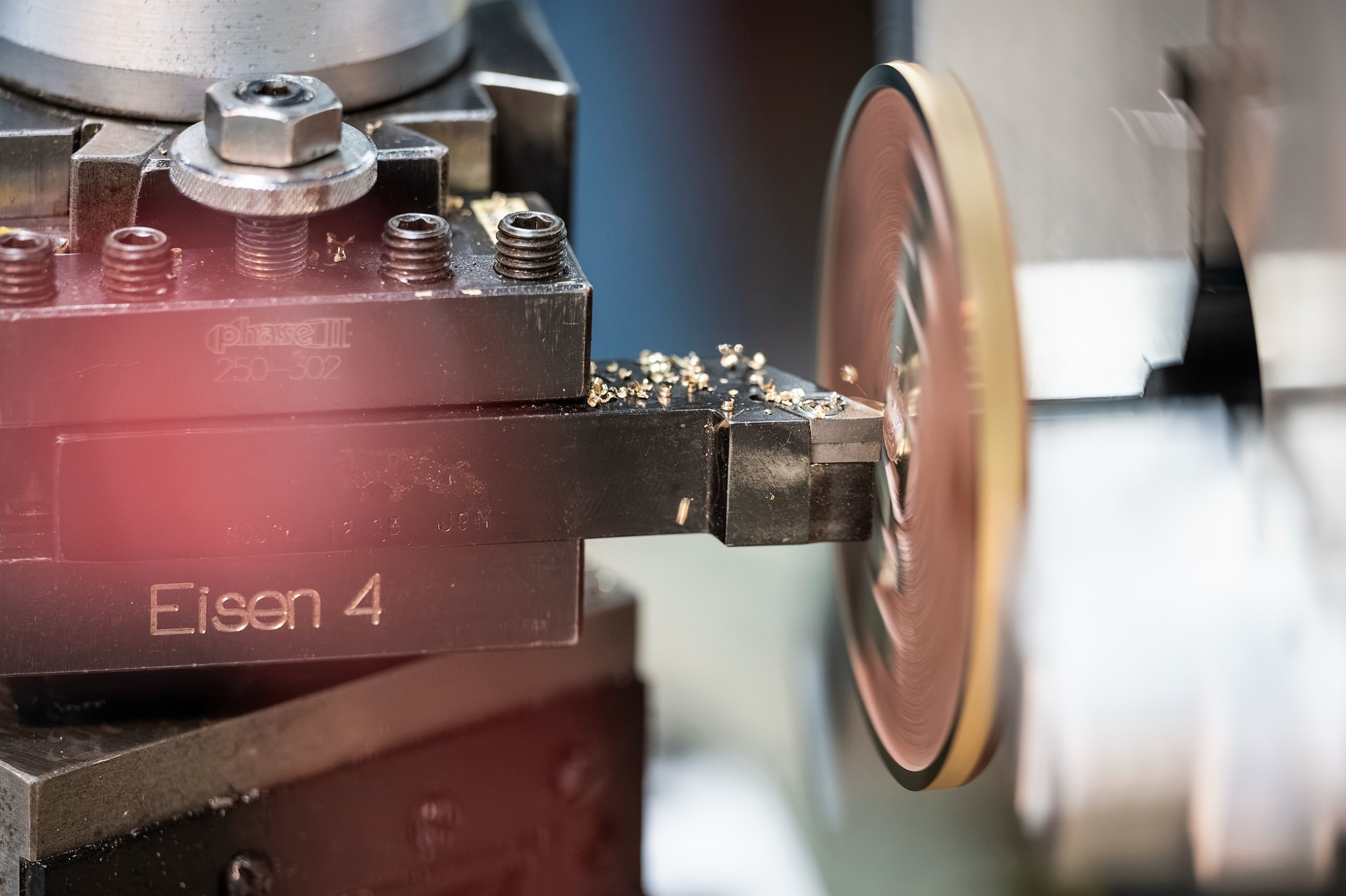 A closeup of a lathe tool machine rotating while cutting a circular piece of metal.