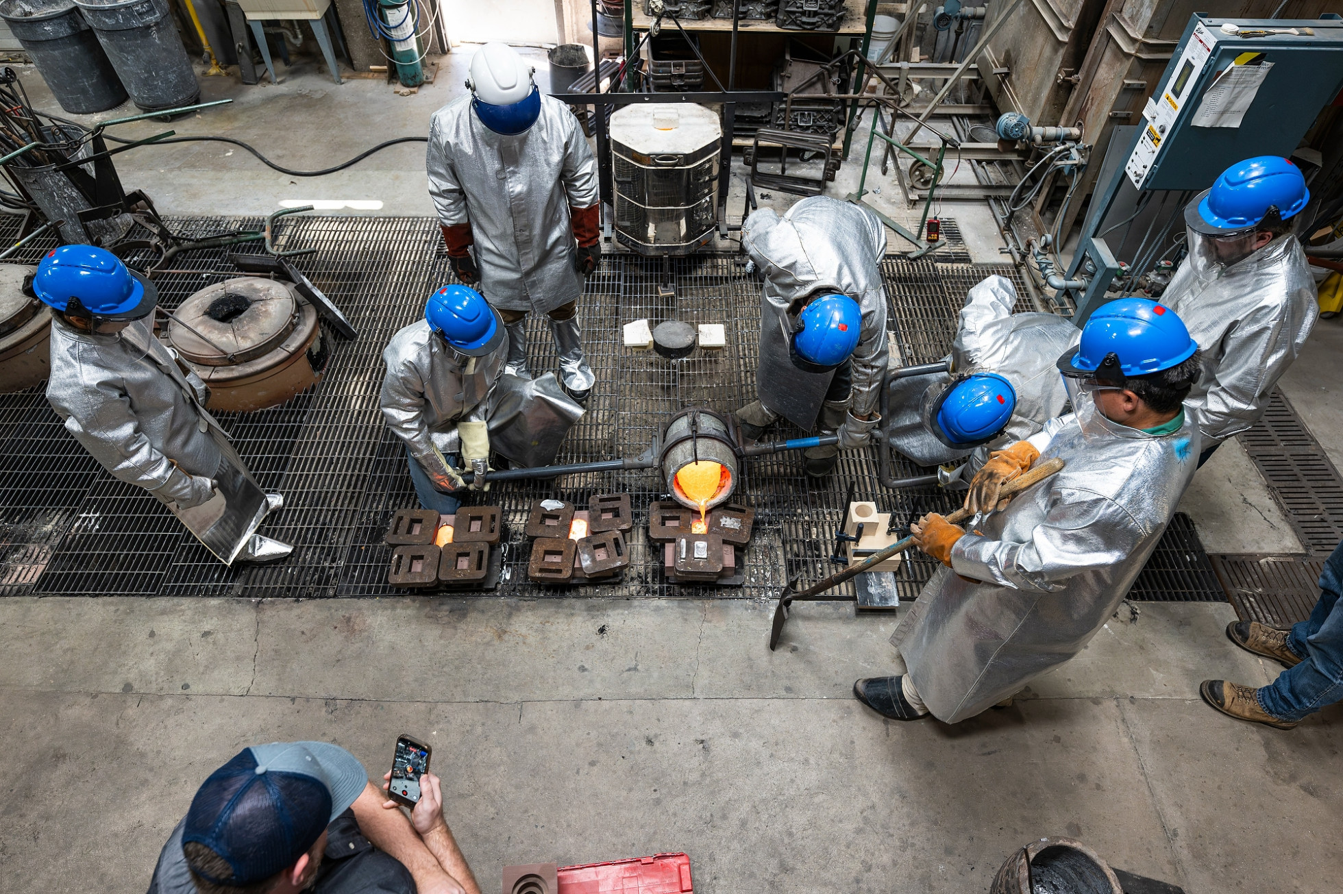 An overhead image of a group of people watching molten metal being poured into a mold.