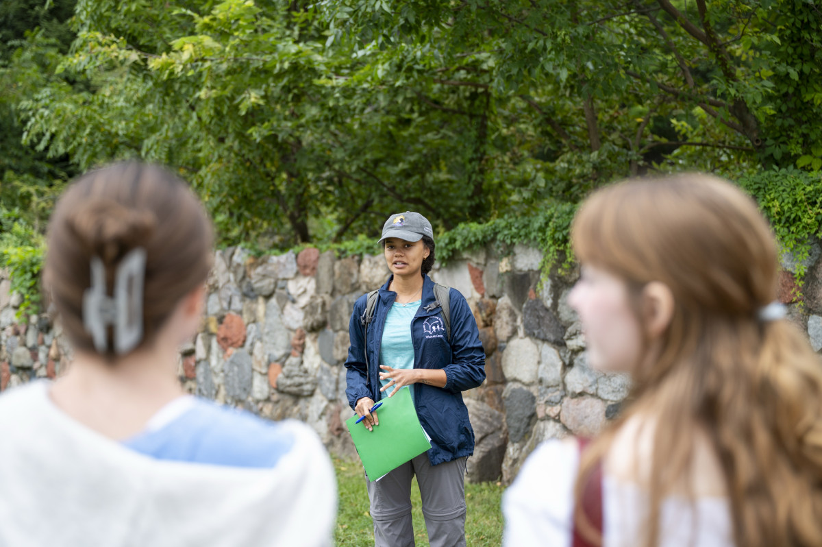 Magomolla holds a bright green folder in one hand while talking to the group of students standing in front of her.