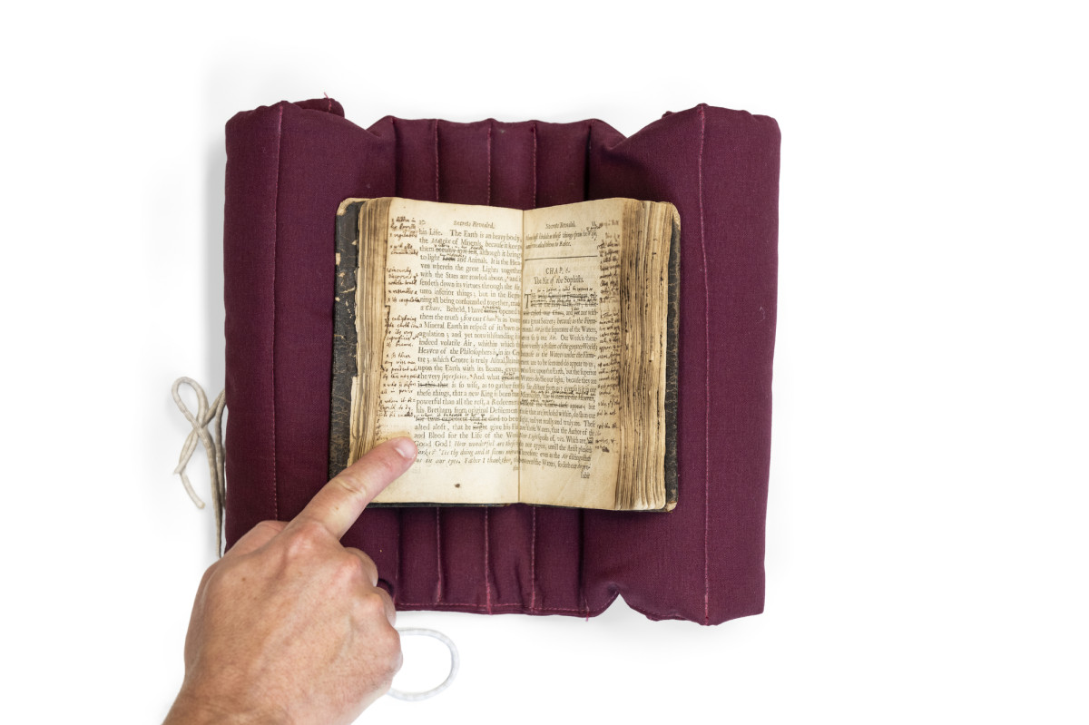 An old book is displayed and held open by a pointer finger.