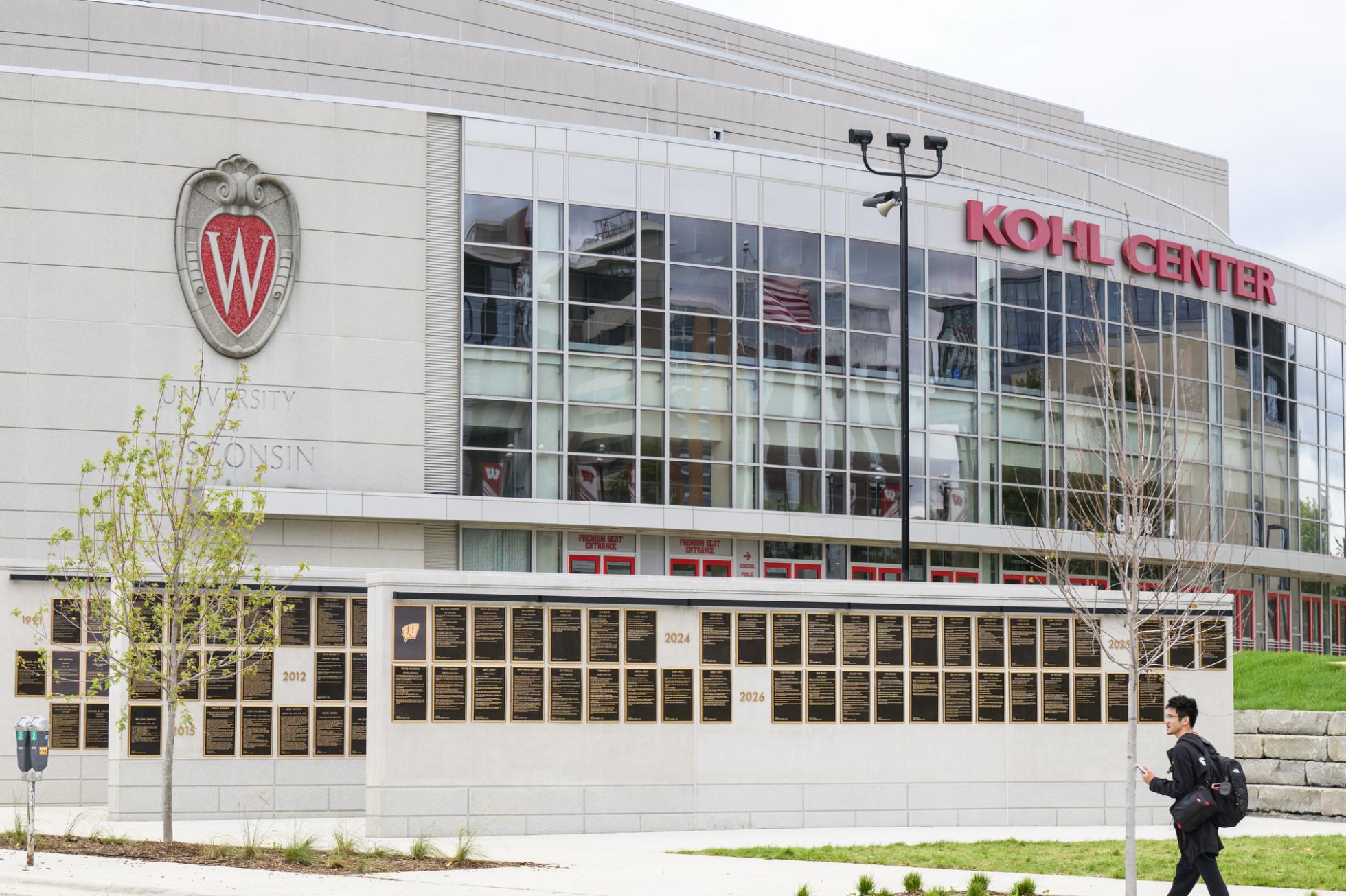 The UW Athletic Hall of Fame installation in front of the Kohl Center, with a person walking by.