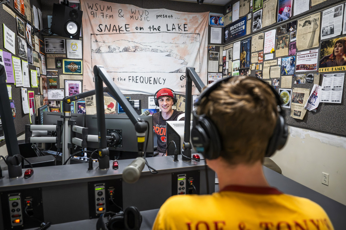 Johnny Raider wearing backwards baseball cap runs a live radio broadcast in the studio surrounded by microphones and radio equipment