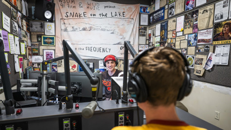 Johnny Raider wearing backwards baseball cap runs a live radio broadcast in the studio surrounded by microphones and radio equipment
