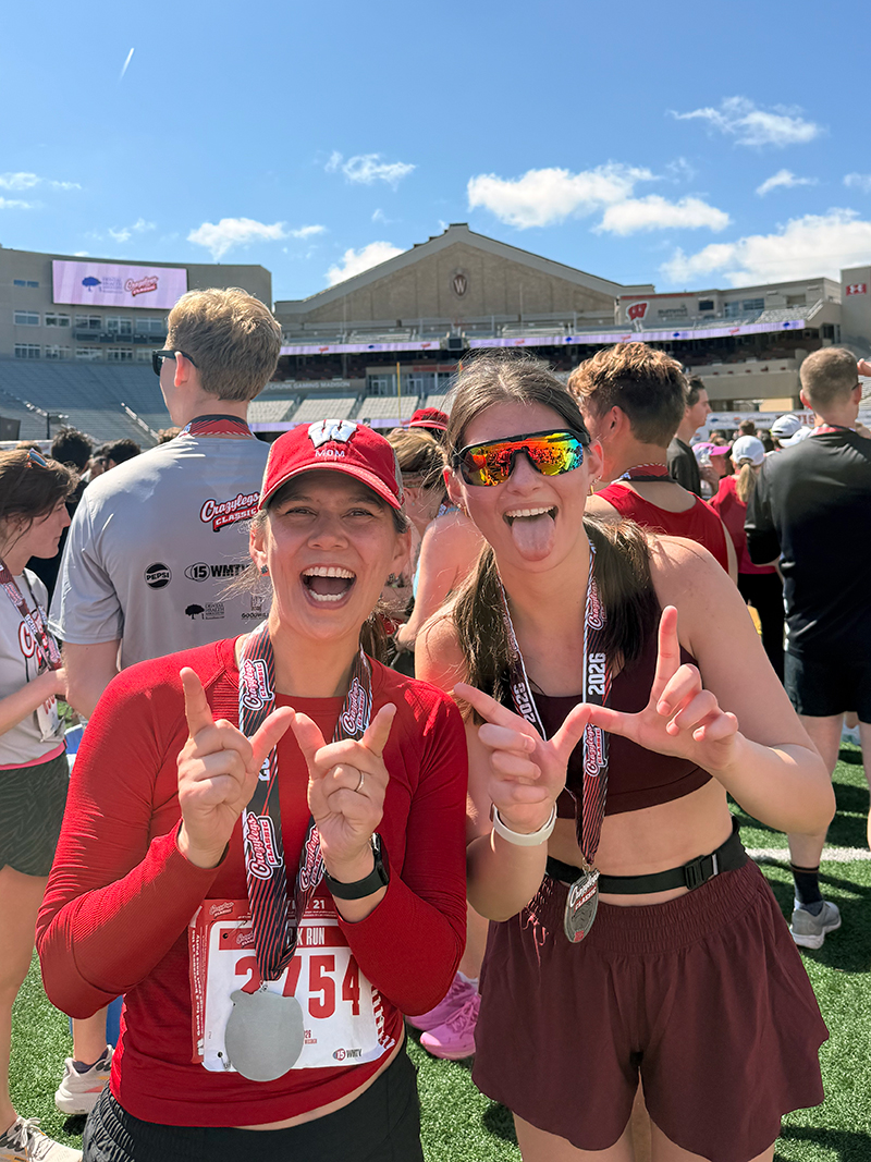 Student Eva Espinoza-Almaza pictured with her mother at Camp Randall stadium. Both people are smiling and making a "W" with their hands