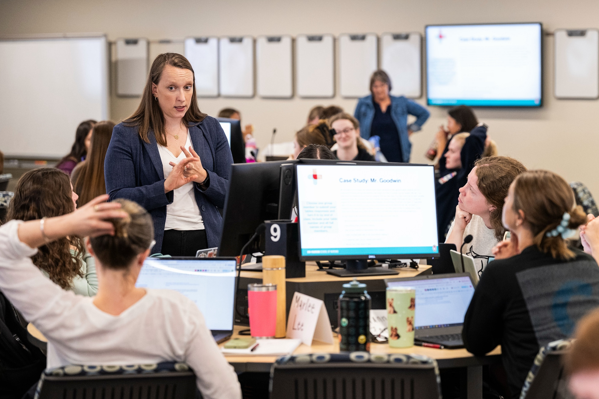 An instructor talks to a group of students seated in front of computer screens.