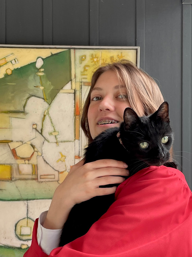 Student Frida Galt holding a black cat with an abstract painting in the background