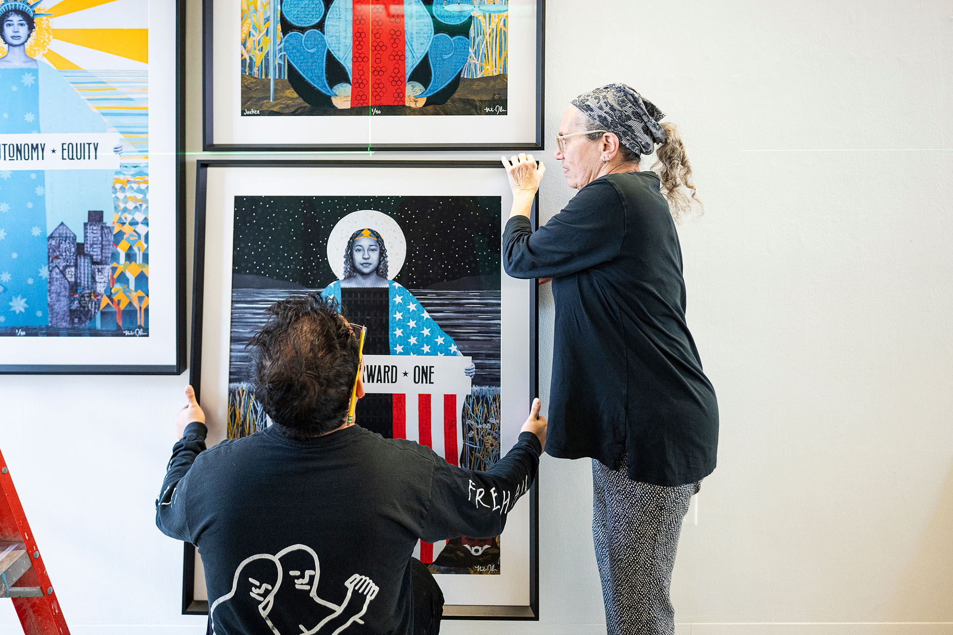 Laurie Beth Clark and Mark Almanza work to hang art pieces on a wall