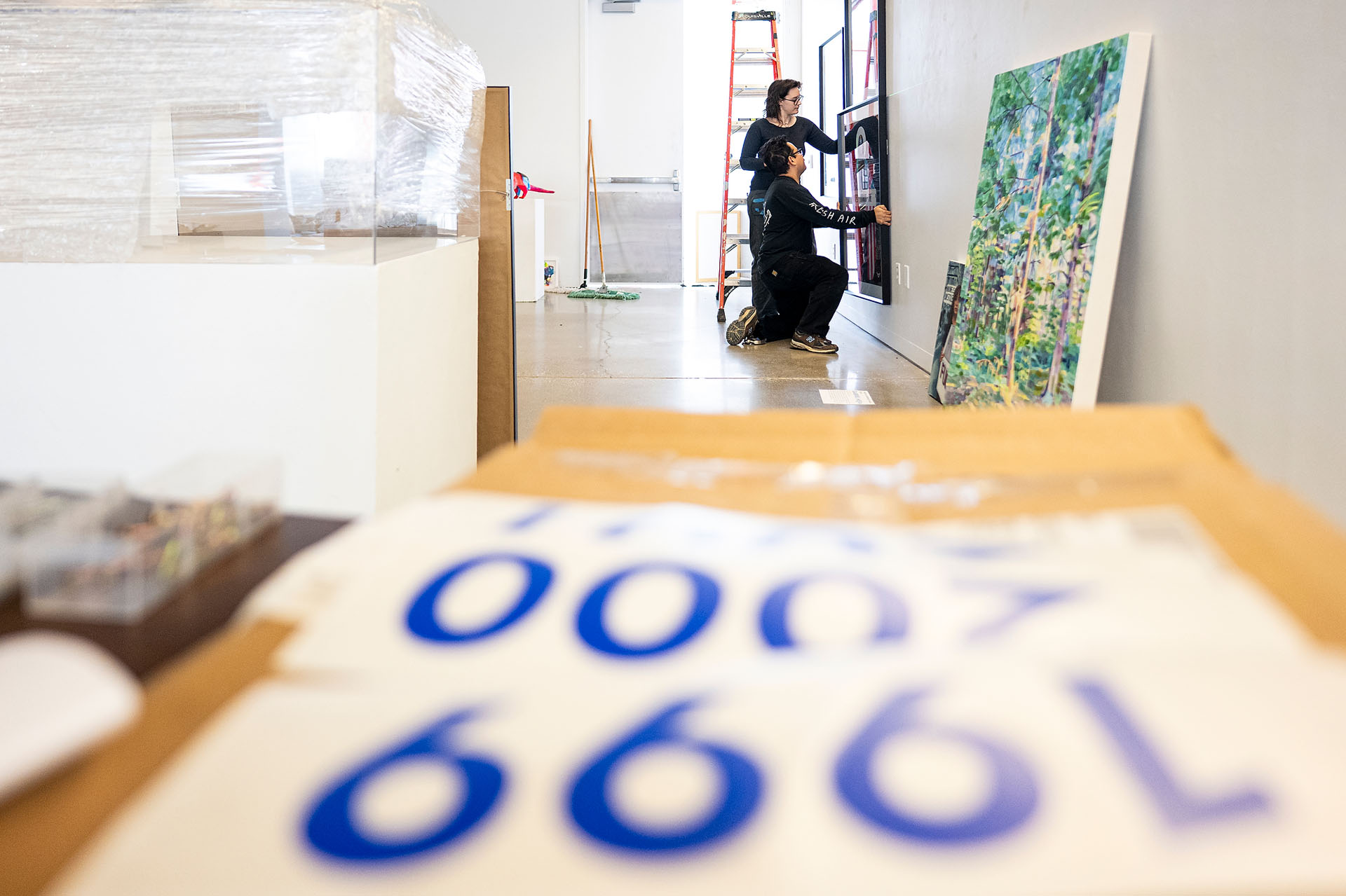 Exhibition installers Mark Almanza and Christian Ulloa work together to hang a painting