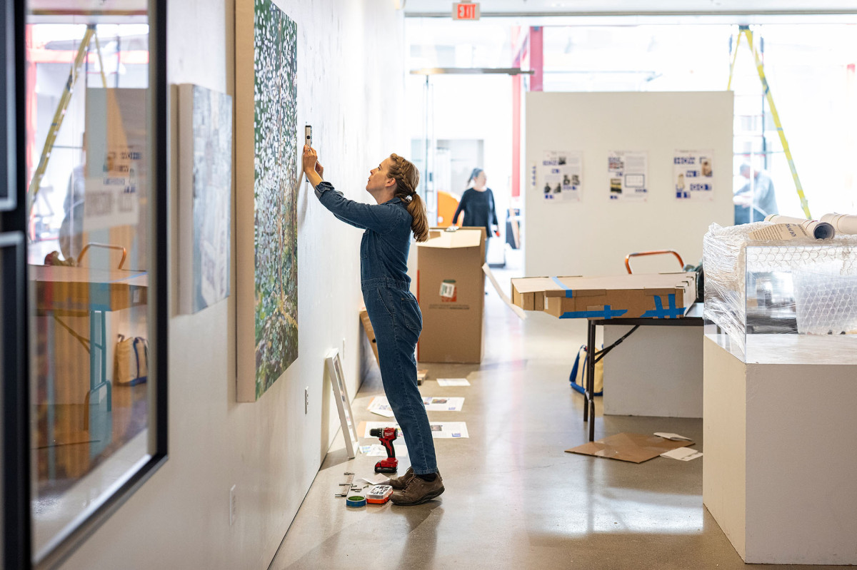Emily Belknap holds a level against a gallery wall in preparation to hang her art