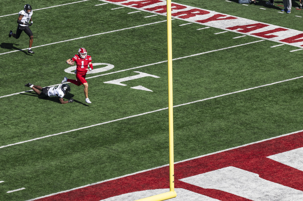 A player wearing a red UW Athletics jersey with the number one misses a tackle and runs with the ball towards the end zone.