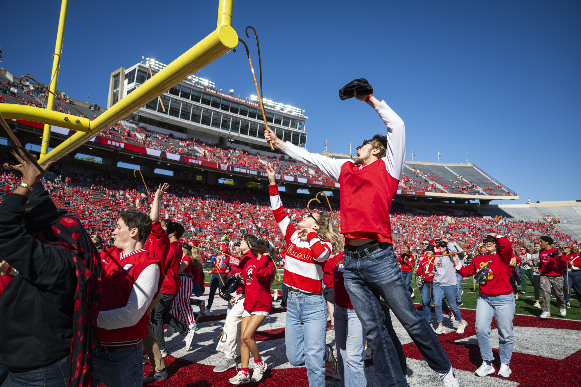 Group of UW students aim wooden canes at the yellow goalposts in Camp Randall Stadium.